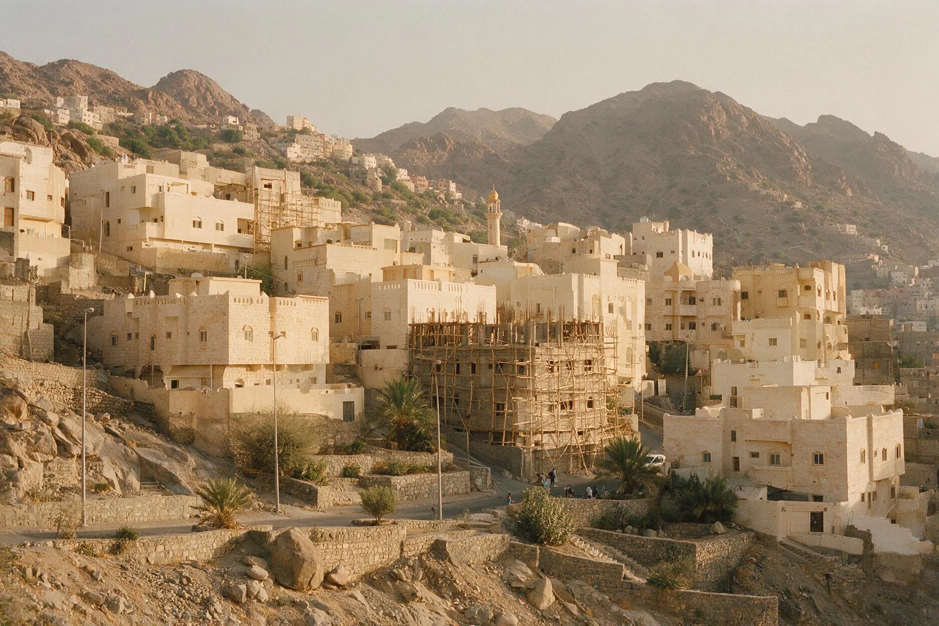 Pale stone apartment buildings stepping up a rocky hillside in Makkah Province, some under construction