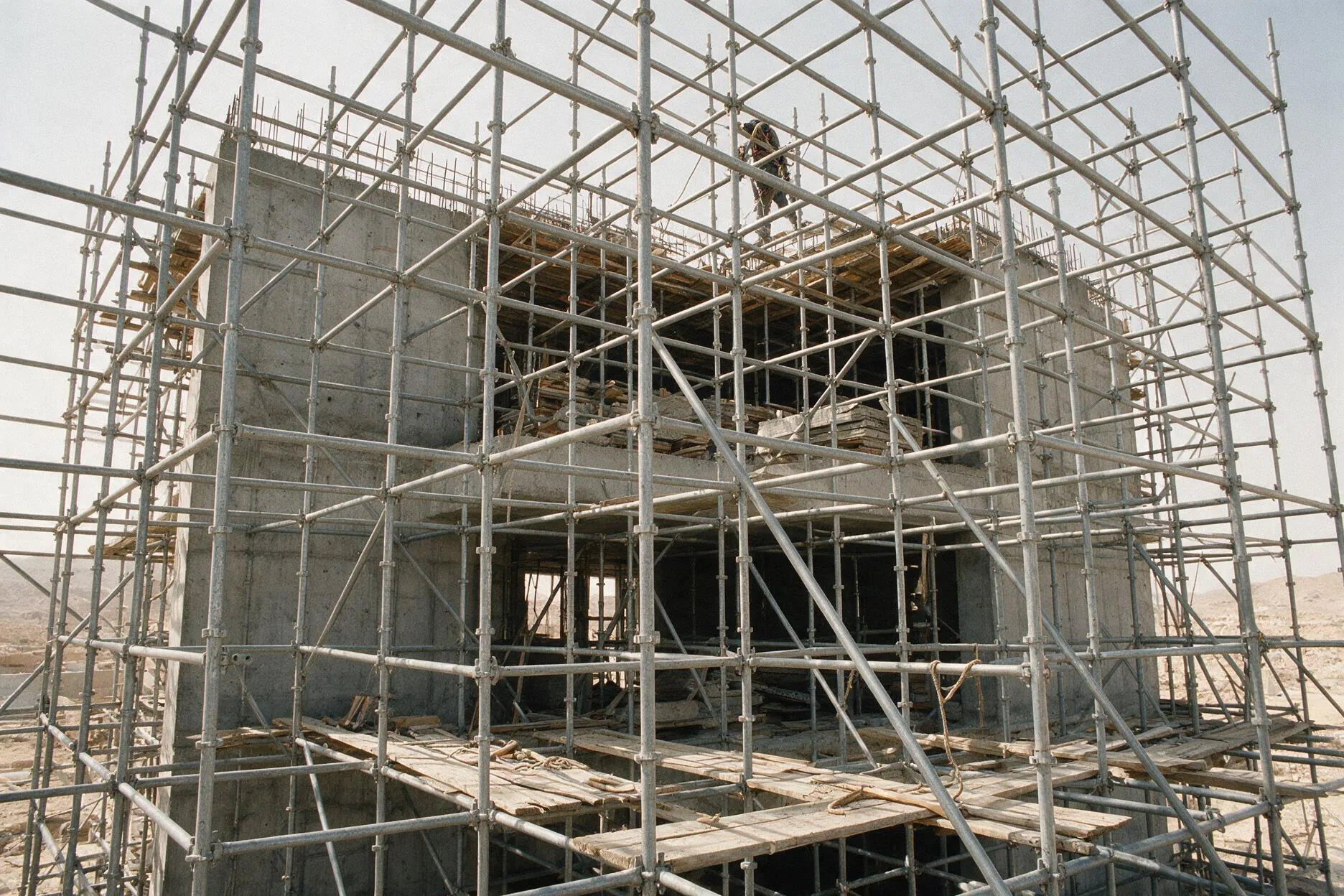 Steel tube-and-fitting scaffold erected around a concrete building, with a scaffolder working the upper lift